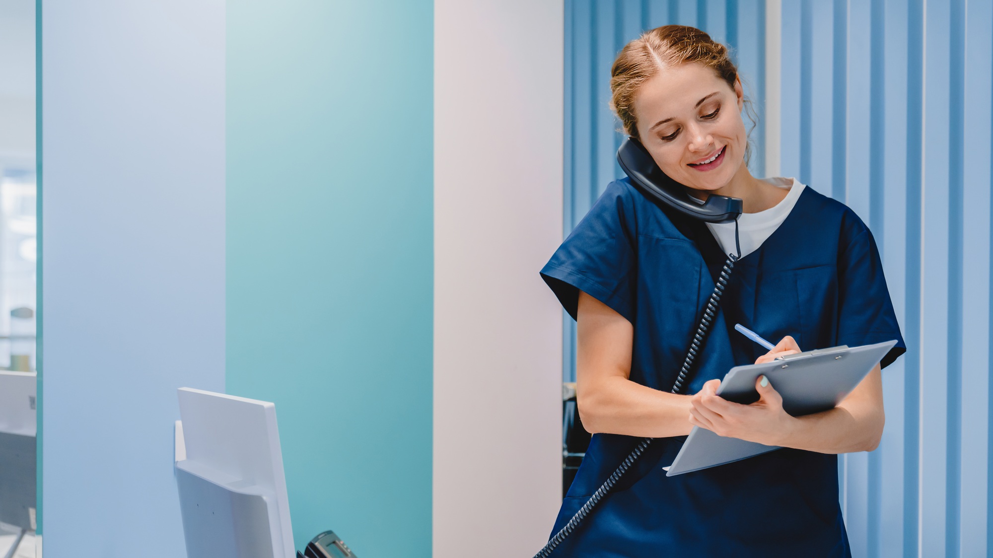 Caucasian female practitioner working at reception desk while answering phone calls